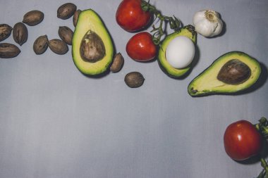 Dilimlenmiş avokado, yumurta, fındık, domates ve gri bir arka plan.