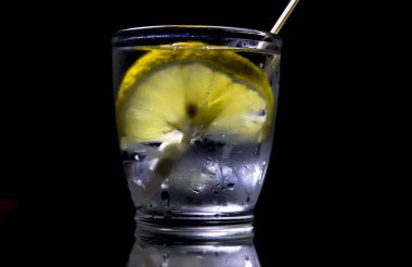 Koyu arkaplanda şeffaf bir bardakta limonlu su..