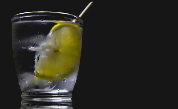 Koyu arkaplanda şeffaf bir bardakta limonlu su..