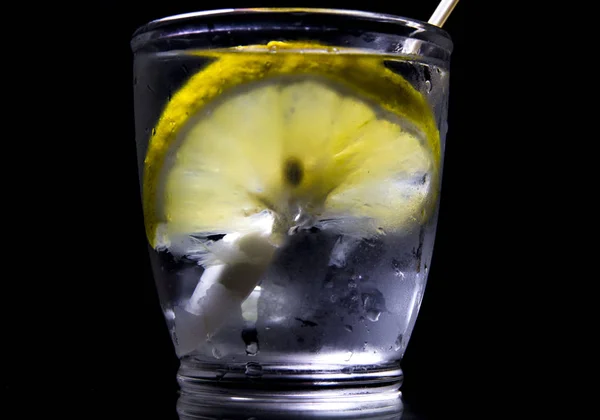 Koyu arkaplanda şeffaf bir bardakta limonlu su..