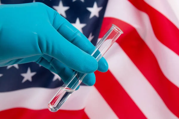 Amerikan bayrağının arka planında tıbbi bir test tüpü tutan eldivenli el.