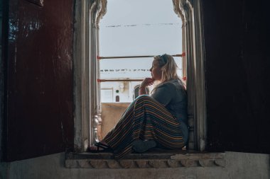 Düşünceli sarışın kadın pencere pervazında oturup düşünüyor. Udaipur Hindistan 'da çekildi