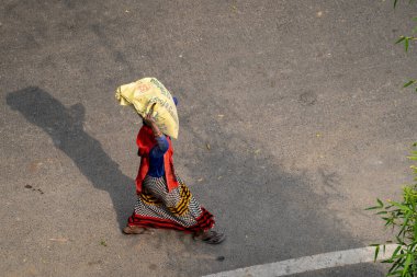 Yeni Delhi, Hindistan - 21 Mart 2020: Kafasında ağır bir çimento torbasını taşırken ve dengede tutarken sari giyen Hintli kadın, bir inşaat alanında çalışıyor.