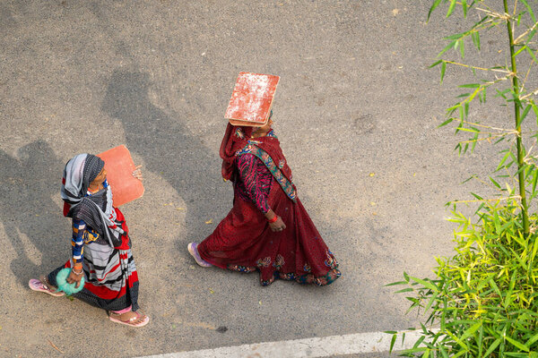 New Delhi, India - March 21, 2020: Two Indian woman walk with empty balancing boards for carrying construction materials on top of head, working at a construction site