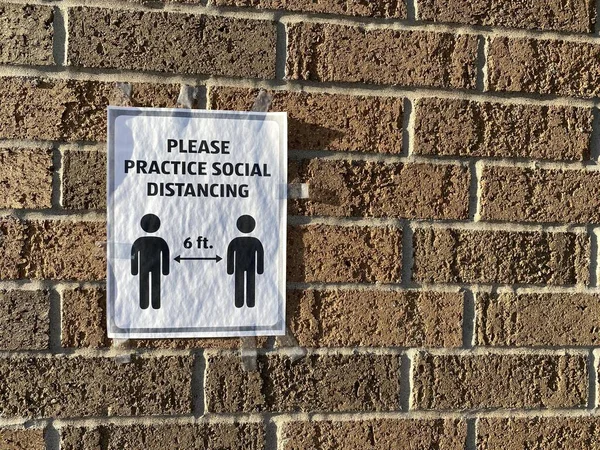 Sign on a brick wall reminds customers to please practice social distancing, standing 6 feet apart, during the Corona Virus pandemic COVID-19 outbreak in the United States of America