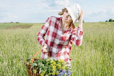 Bir kız alanında toplar çiçekler, alan Çiçek sepet içinde a capella kırmızı bir kutu, kot gömlek ve içinde bir gömlek giymiş bir gülümseme ile genç bir kız, o gider ve renkli (mavi ve sarı) çiçek yeşil alana (çayır tatili).