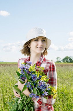 Bir kız alanında toplar çiçekler, alan Çiçek sepet içinde a capella kırmızı bir kutu, kot gömlek ve içinde bir gömlek giymiş bir gülümseme ile genç bir kız, o gider ve renkli (mavi ve sarı) çiçek yeşil alana (çayır tatili).