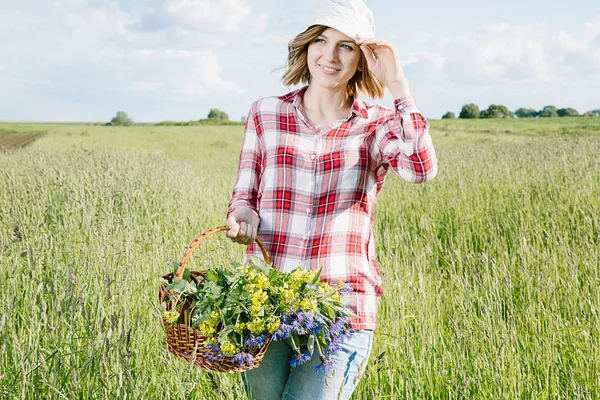 Bir kız alanında toplar çiçekler, alan Çiçek sepet içinde a capella kırmızı bir kutu, kot gömlek ve içinde bir gömlek giymiş bir gülümseme ile genç bir kız, o gider ve renkli (mavi ve sarı) çiçek yeşil alana (çayır tatili).