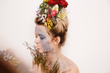 Onun kafası ve elleri üzerinde çiçekler olan bir genç kadın. Çiçekli bahar görüntü. Renkli bir bitki olan adam. Kız ve çiçek açan saç kesimi ve brokar yüzünde.