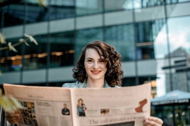 Genç bir kadın gazete ve kitap okuyor, gülümsüyor. Varşova, Polonya