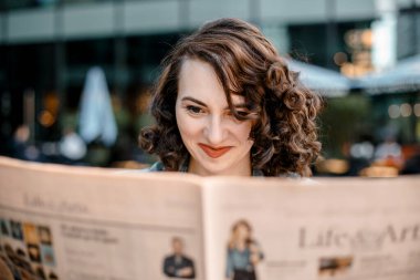 Genç bir kadın gazete ve kitap okuyor, gülümsüyor. Varşova, Polonya