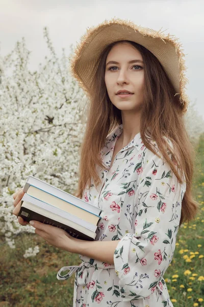 Girl reading a book in the spring garden. Gorgeous woman in hat and dress on nature. Camping with a book. Spring. Summer.