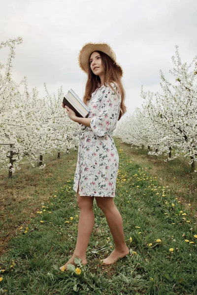 Girl reading a book in the spring garden. Gorgeous woman in hat and dress on nature. Camping with a book. Spring. Summer.