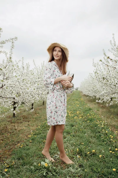 Girl reading a book in the spring garden. Gorgeous woman in hat and dress on nature. Camping with a book. Spring. Summer.