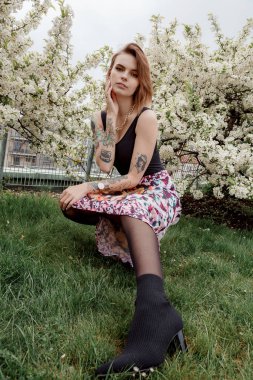 Çiçekli çalıların yanındaki beyaz elbiseli şık kız. Moda pozu.
