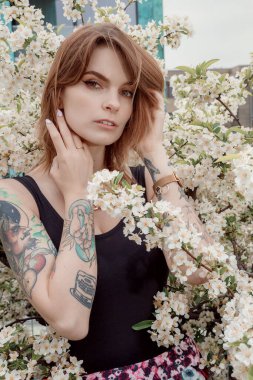 Çiçekli çalıların yanındaki beyaz elbiseli şık kız. Moda pozu.