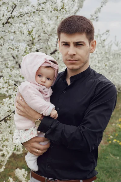 Jovem pai com a sua filha recém-nascida. Pai e filha perto de uma árvore florida . — Fotografia de Stock