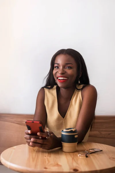 Smiling black girl chatting by smartphone at cafe.