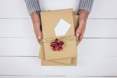 Beyaz ahşap arka planda hediyeler tutan gri kazaklı bir kadın eli. Noel, yeni yıl, doğum günü, sevgililer günü, anneler günü konsepti. Üst görünüm.