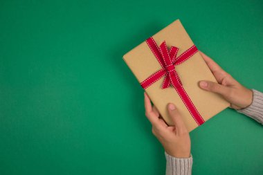 Yeşil arka planda kırmızı kurdeleli bir hediye tutan bir kadının elleri. Noel, yeni yıl, doğum günü, sevgililer günü, anneler günü konsepti. Uzayı kopyala Üst görünüm.
