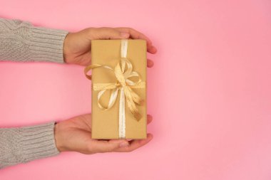 Gri kazaklı bir kadının elleri pembe arka planda altın bir fiyonk taşıyan bir hediye tutuyor. Noel, yeni yıl, doğum günü, sevgililer günü, anneler günü konsepti. Uzayı kopyala Üst görünüm.