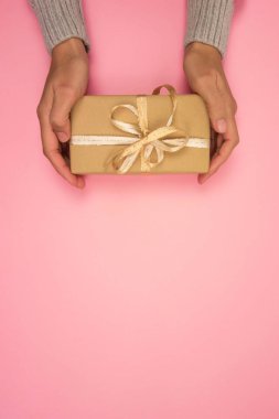 Gri kazaklı bir kadının elleri pembe arka planda altın bir fiyonk taşıyan bir hediye tutuyor. Noel, yeni yıl, doğum günü, sevgililer günü, anneler günü konsepti. Uzayı kopyala Üst görünüm.