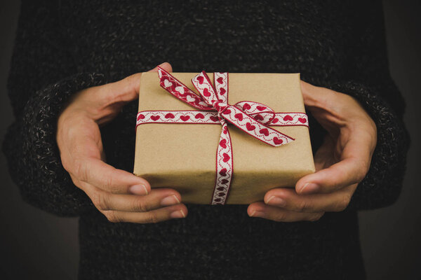 Женщина в тёмном свитере держит подарок с сердечным луком. Чёрный фон. Рождество, Новый год, день рождения, День Святого Валентина, концепция Дня матери
.