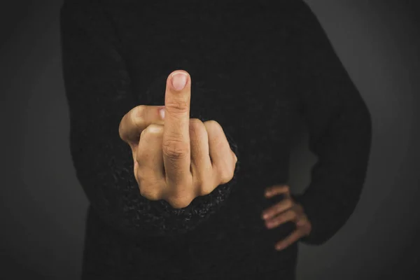 Woman with dark sweater showing middle finger. Black background.