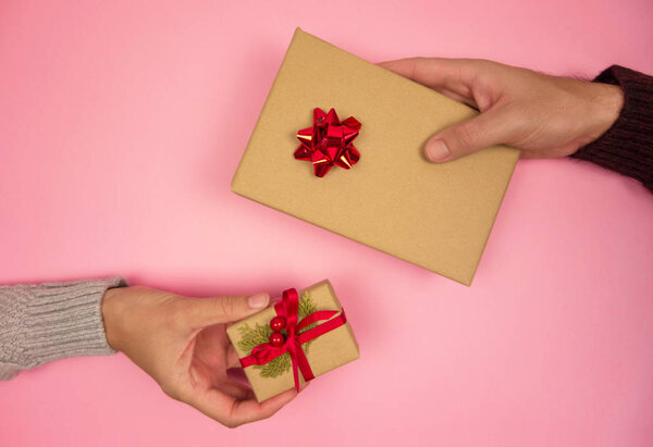 Рука женщины и мужчины обмениваются рождественскими подарками на розовом фоне. Вид сверху
.