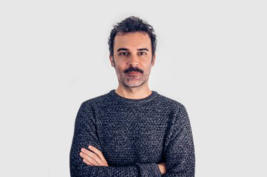 Kahverengi, gülümseyen, bıyıklı ve kolları çapraz duran gri kazaklı yakışıklı bir adam portresi. Gri arkaplan.