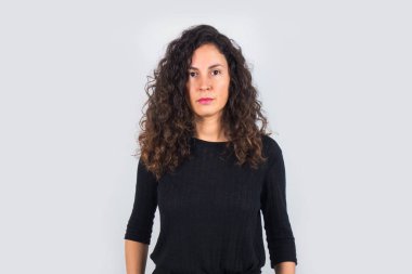 Kıvırcık saçlı esmer kadın ve siyah gömlek kameraya ciddi ciddi bakıyor..