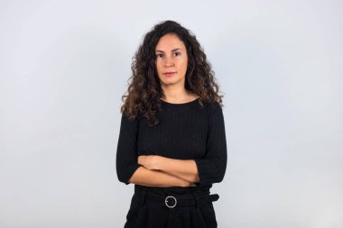 Kıvırcık saçlı esmer kadın ve siyah gömlekli, kolları çapraz ve kameraya bakıyor..
