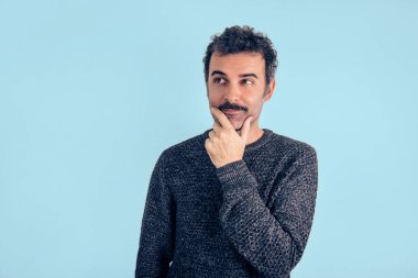 Bıyıklı ve gri kazaklı yakışıklı ve kahverengi düşünen bir adamın portresi. Gri arka plan. Boşluğu kopyala