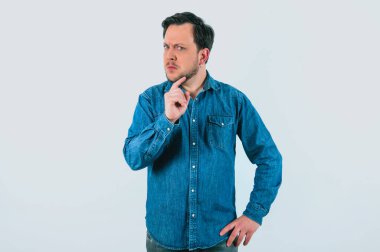 Fikir ayrılığı ve kararlılık ifadesi olan genç bir adam. Denim gömlek ve izole edilmiş beyaz arkaplan.