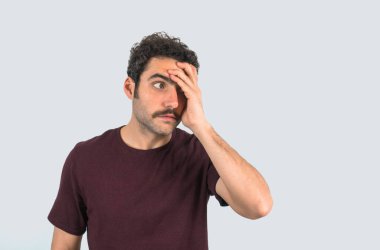 Bıyıklı, yüzünde huzursuzluk jesti olan genç bir adamın portresi. Mor tişört ve izole edilmiş gri arkaplan.