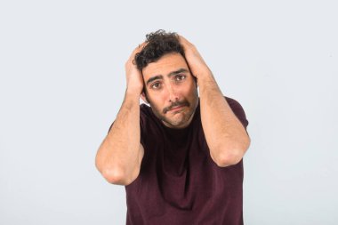 Yorgunluk, üzüntü ve ellerinin başının üzerinde olduğu bıyıklı genç bir adam. Mor tişört ve izole edilmiş gri arkaplan.