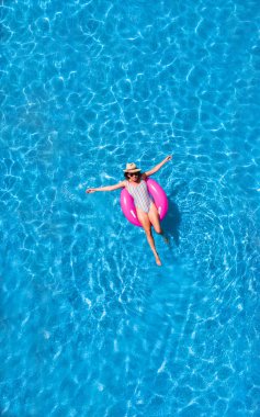 Yazın yüzme havuzu manzarası. Pembe donutla süzülen mayo ve şapkalı genç kız..