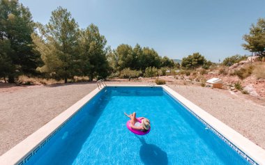 Yazın havuz manzarası. Pembe donutla süzülen mayo ve şapkalı genç kız..