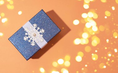 Turuncu zemininde kar taneleri olan mavi, parlak bir Noel hediyesi. Bir şenlik kompozisyonu.