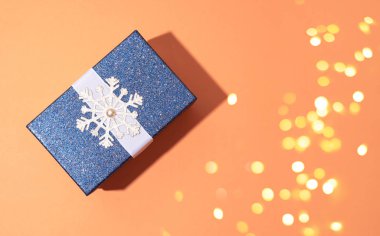 Turuncu zemininde kar taneleri olan mavi, parlak bir Noel hediyesi. Bir şenlik kompozisyonu.