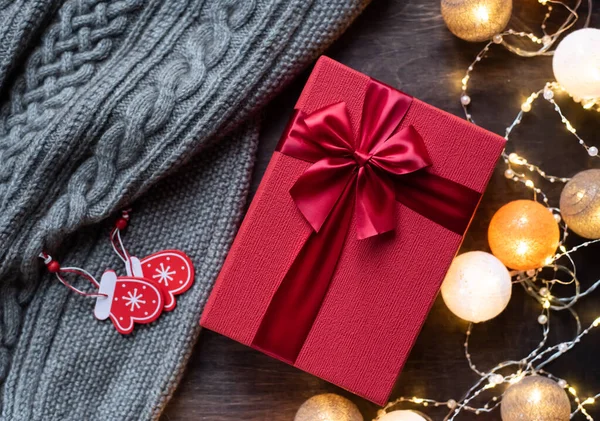 Coffret cadeau rouge avec noeud sur fond bois foncé. Guirlande festive avec lumières . — Photo