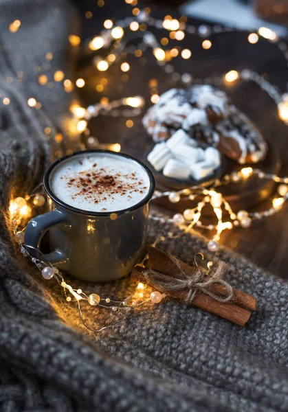 Cup of coffee with cinnamon. Christmas background with lights, warm knitted scarf. — Stock Photo, Image