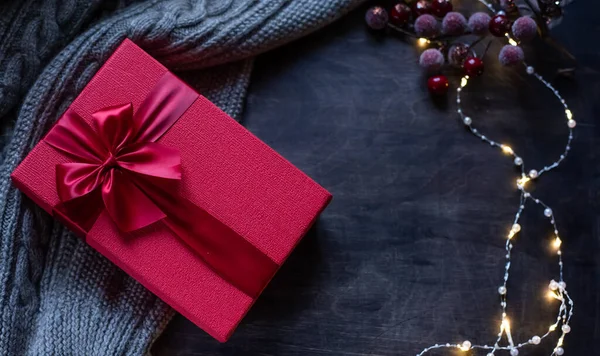 Caja de regalo roja con lazo sobre fondo de madera oscura. Guirnalda festiva con luces . — Foto de Stock