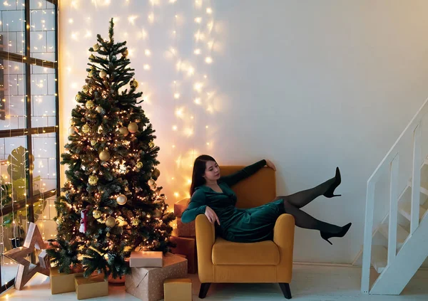 クリスマスツリーの椅子に座っているドレスのエレガントな女性. — ストック写真