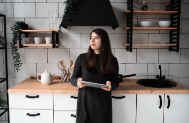 Mutfakta genç bir kadın tabletteki bir şeye bakıyor. Modern beyaz mutfak.