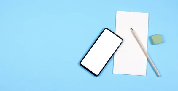 Ein modernes Smartphone liegt auf einem Notizblock, neben Bleistift und Radiergummi. blauer Hintergrund. — Stockfoto