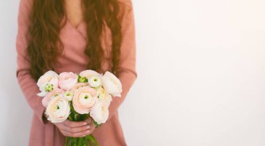 Pembe elbiseli bir kız elinde bir buket narin Ranunculus çiçeği tutuyor. Romantik fotoğraf.