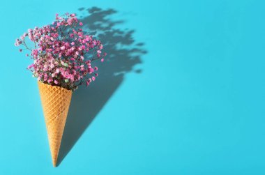 Mavi arka planda küçük bir buket. Pembe çiçekler. Dondurmadan waffle fincanı.
