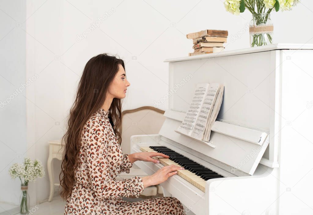 Beautiful young woman with dark long hair at the piano. White room, white piano.