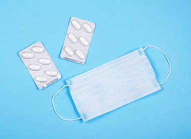 C oronavirüsünün P intikamı. Tıbbi maskeler, mavi arka planda vitaminler..